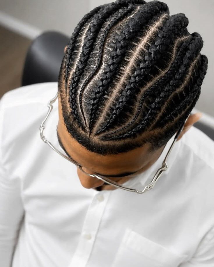 Man with neat black cornrow braids wearing a white shirt and silver glasses.