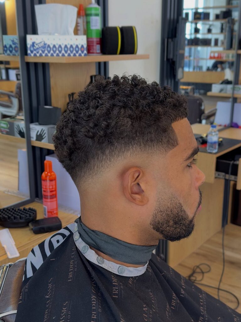 Man with curly hair and a beard showing a fresh skin fade haircut.