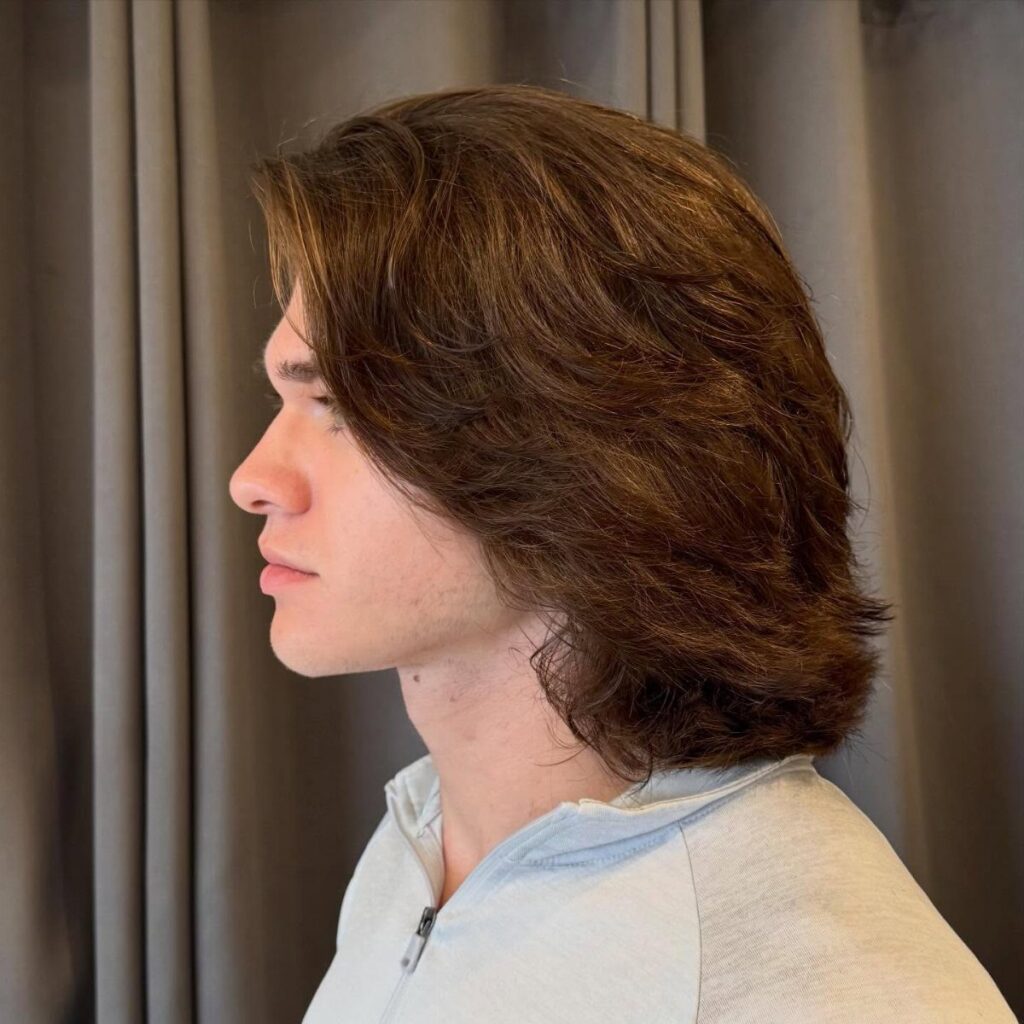 Young man with long wavy brown hair seen from a side profile view.