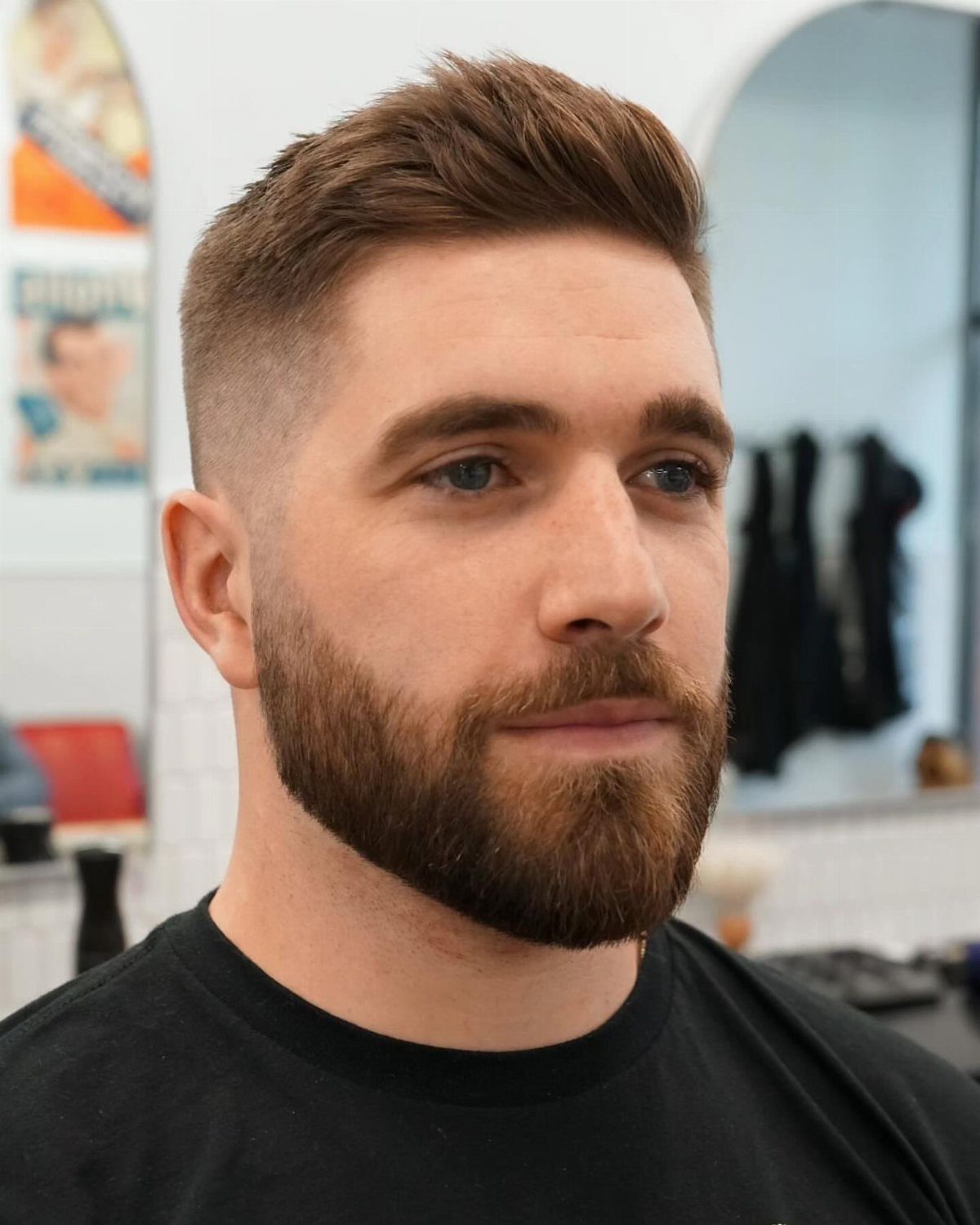 Man with a groomed brown beard and a short faded haircut in a barbershop