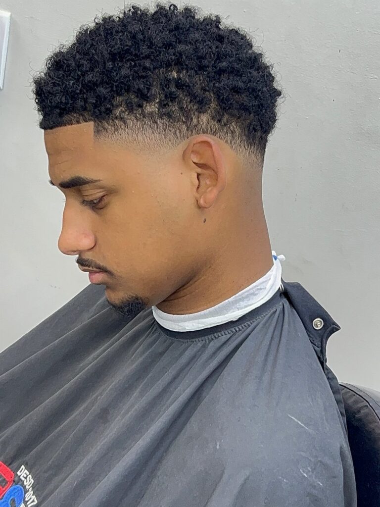 Man with curly black hair and a high taper fade haircut wearing a cape.