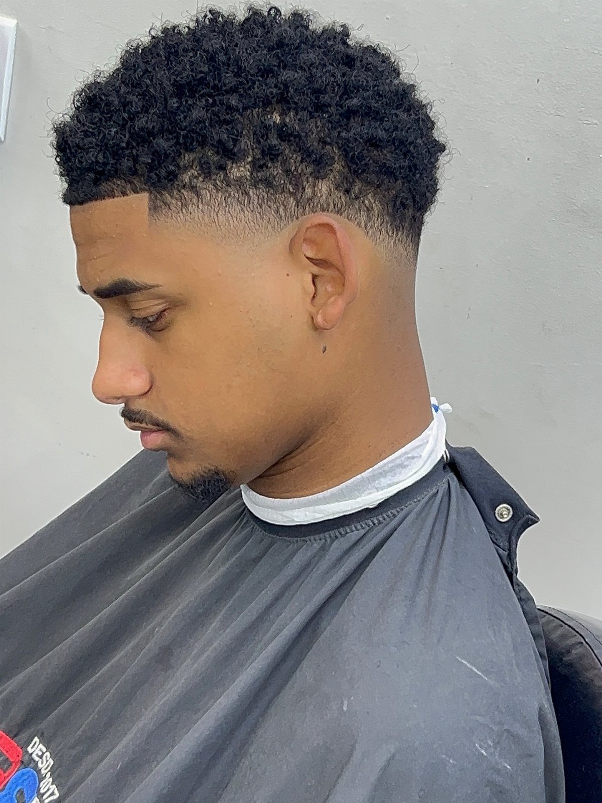 Man with curly black hair and a high taper fade haircut wearing a cape.