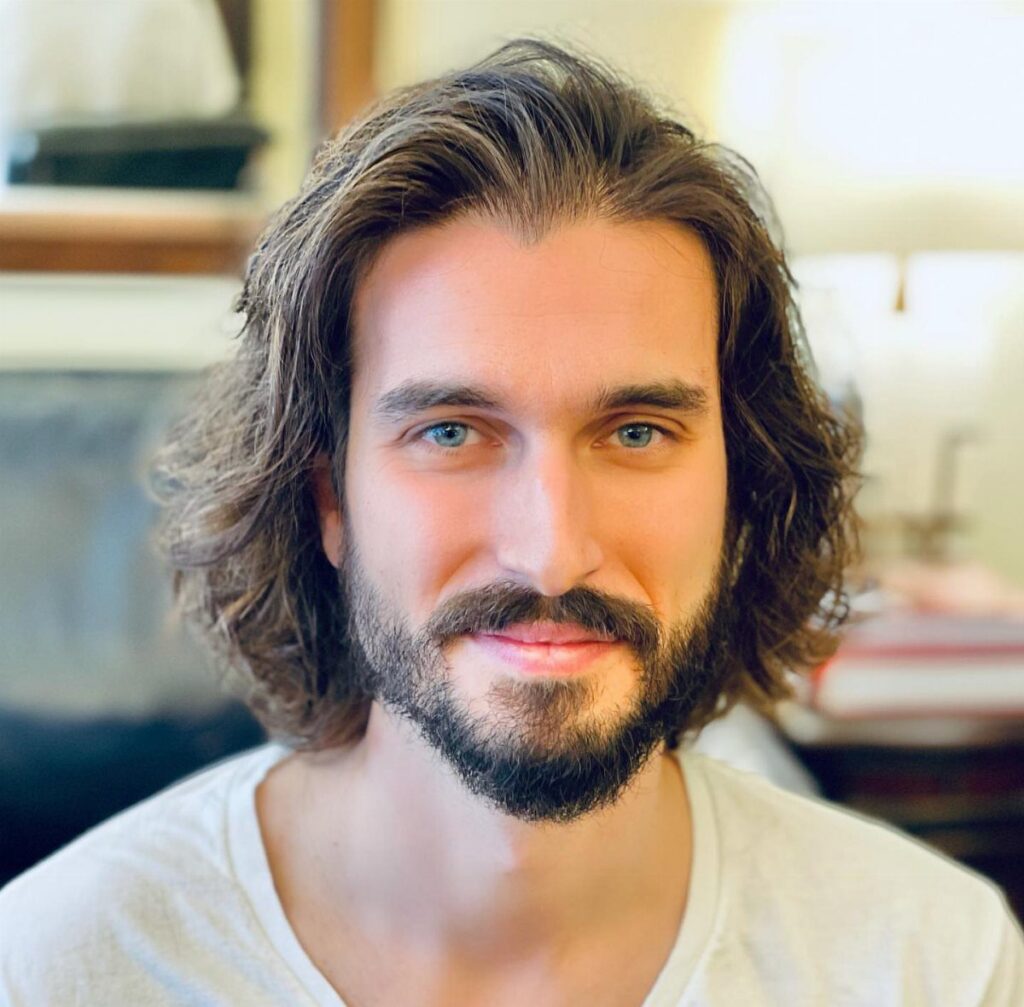 Man with shoulder-length wavy brown hair and a full groomed beard.