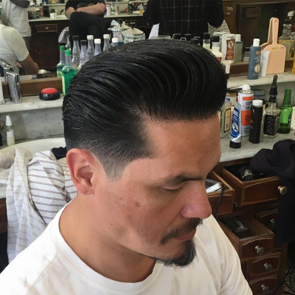 Man with a high-volume pompadour hairstyle in a barbershop setting.