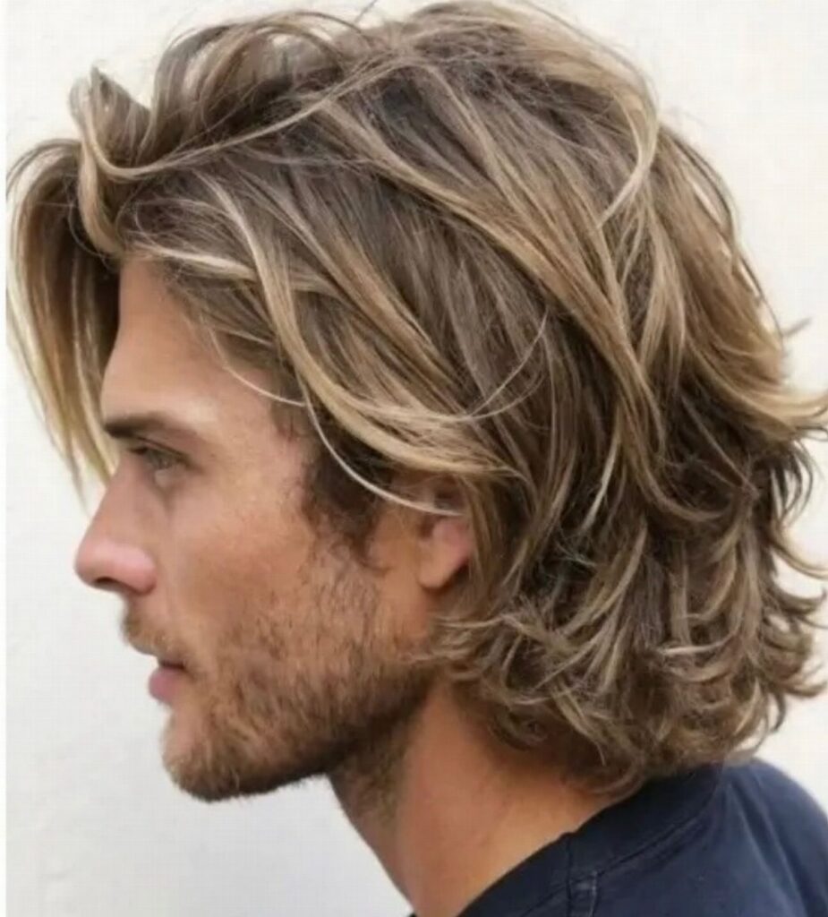 Man with wavy medium length blonde hair and a beard in side profile