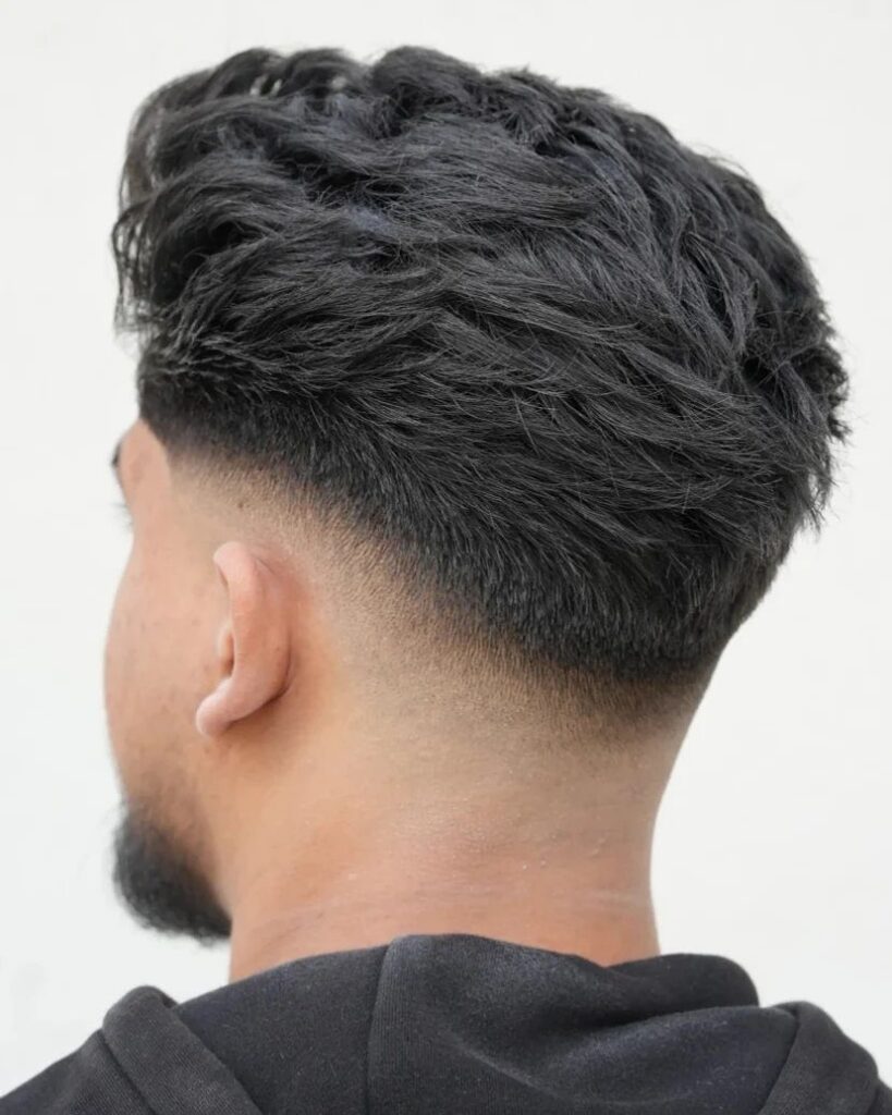 Man with dark wavy hair and a low fade haircut seen from the side.