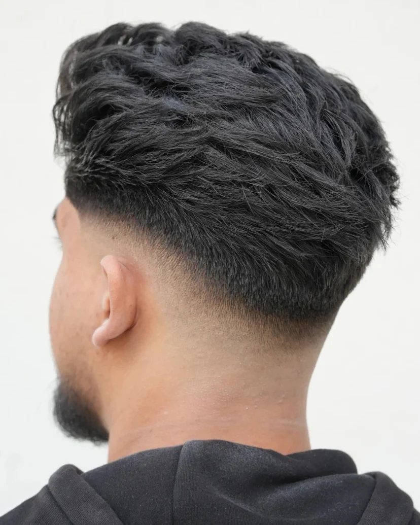 Man with dark wavy hair and a low fade haircut seen from the side.