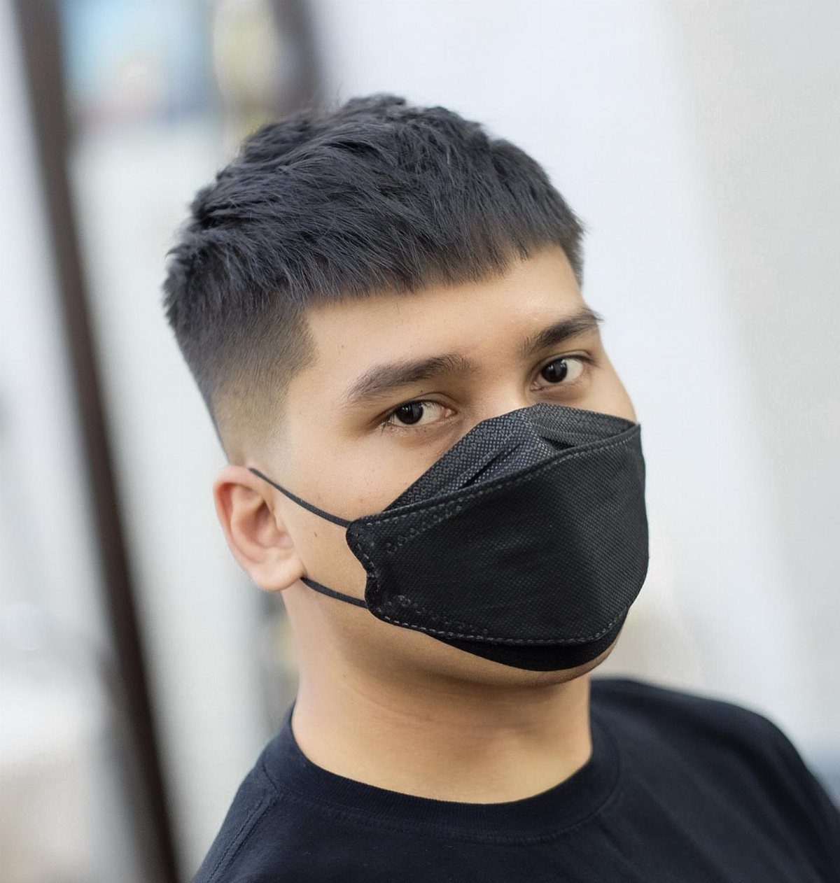 Man with a short straight haircut and fade wearing a black face mask