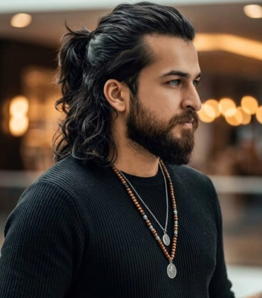 Man with long dark wavy hair in a half-ponytail and a full beard.