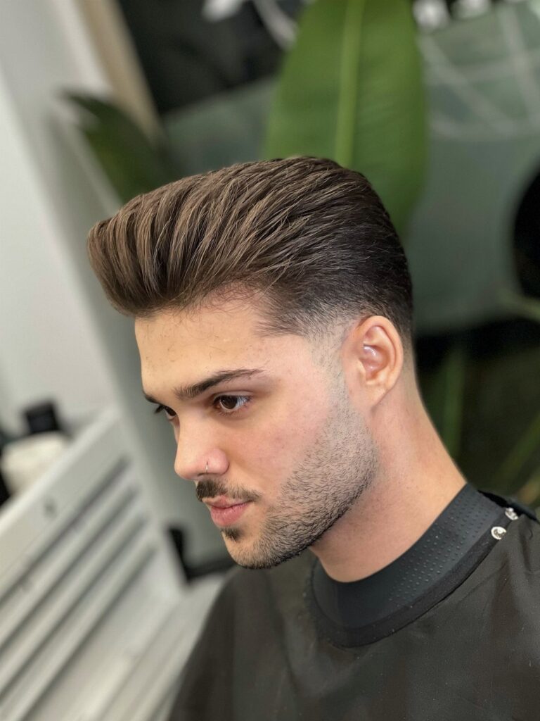 Man with a brown medium pompadour hairstyle and groomed beard in a salon