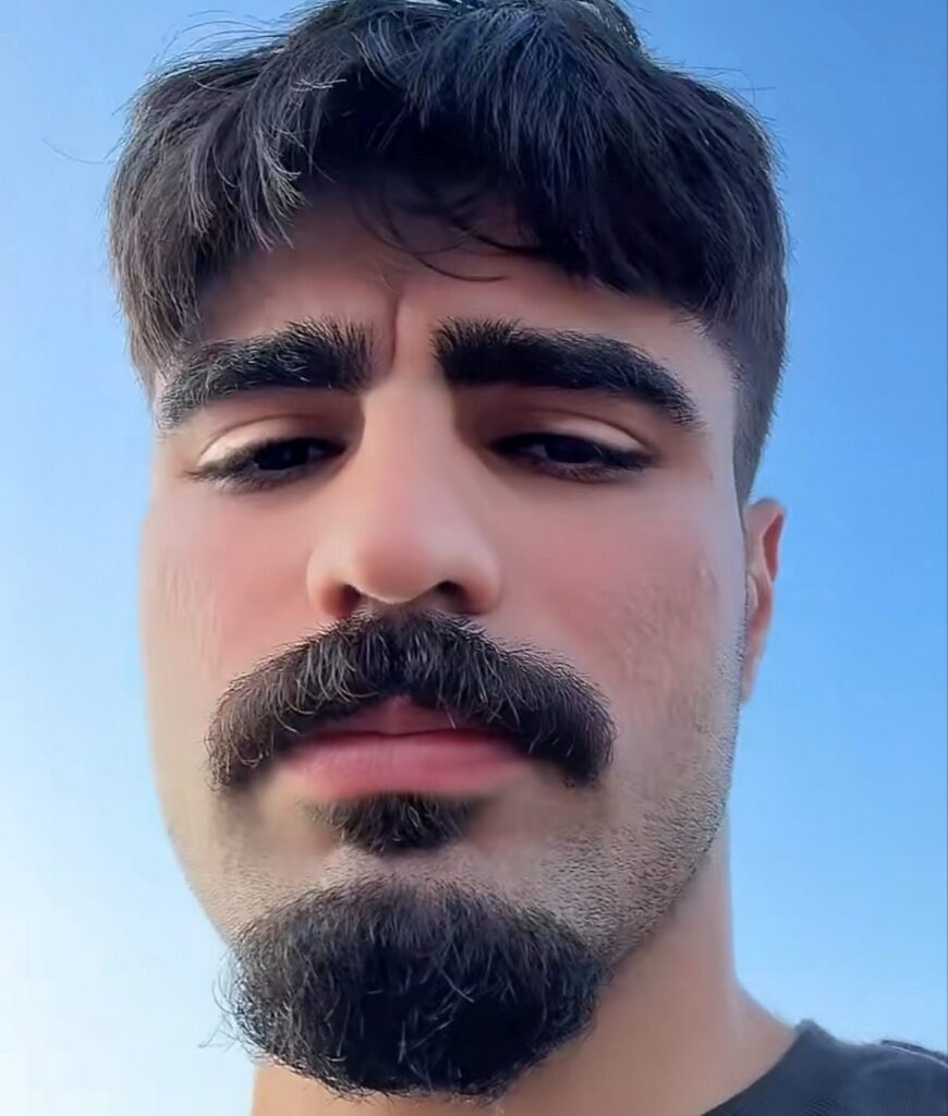 Man with a thick dark mustache and a groomed goatee against blue sky