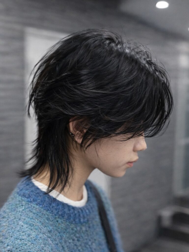 Person with a black short wolf cut hairstyle and blue knit sweater.